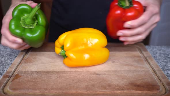 close-up of person putting red green and yellow peppers on a wooden board in the kitchen