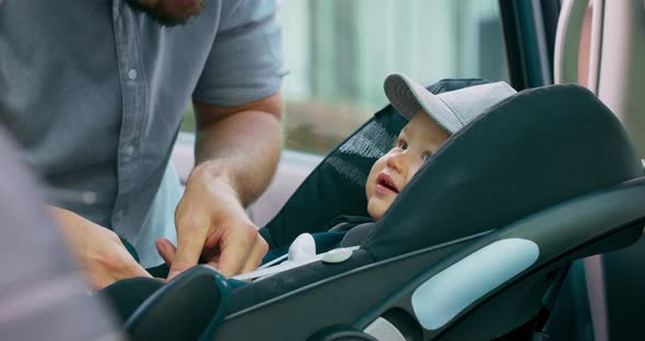 Closeup Baby Boy in Cap Who Sits in the Baby Car Seat Inside of Family Car Door Opens and His