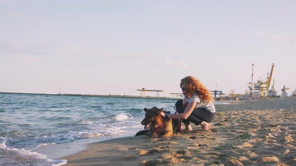 Happy Young Woman Have a Rest with Her German Shepherd Dog Outdoor on the Beach