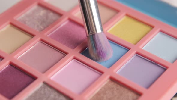 Make-up artist picks up blue pigment from bright colorful eyeshadow palette with a brush.