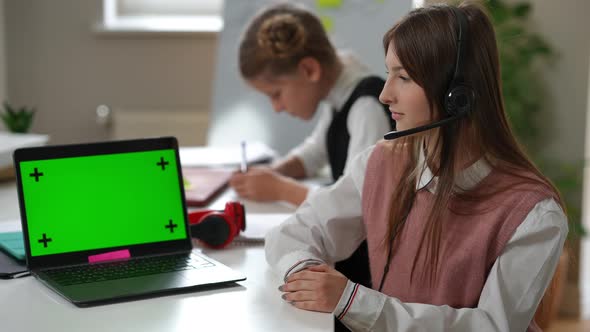 Confident Caucasian Intelligent Schoolgirl Looking at Camera Sitting with Green Screen Laptop at