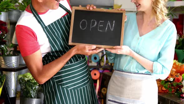 Smiling florists holding open sign on slate in flower shop