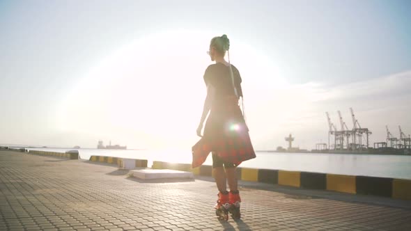 Young Stylish Funky Girl with Green Hair Riding Roller Skates and Dancing Near Sea Port During