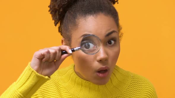 Surprised Black Female Looking Camera Through Magnifying Lens, Shocking News