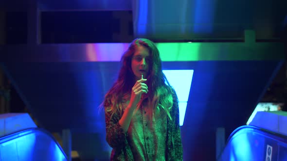 Young woman vaping on an escalator with neon lights