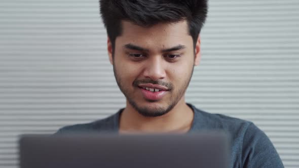 Pretty Indian man wearing t-shirt working on laptop