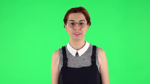 Portrait of Funny Girl in Round Glasses Is Laughing While Looking at Camera. Green Screen
