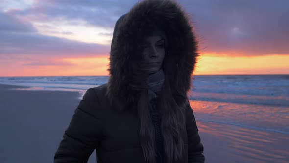 Young woman in winter clothes walks along the sandy shore of the Baltic sea beach at romantic sunset
