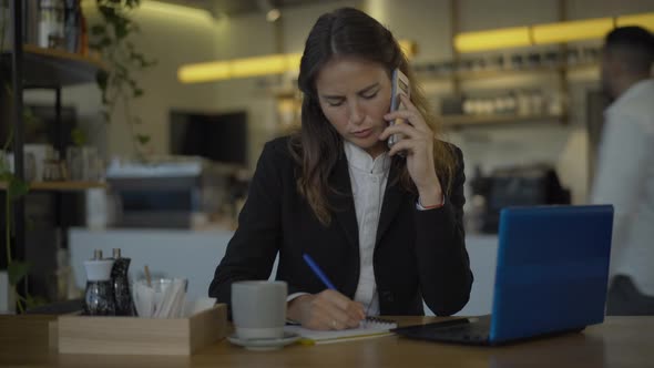 Young Female CEO Talking on the Phone Sitting at the Table in Cafe and Hanging Up. Portrait of Busy