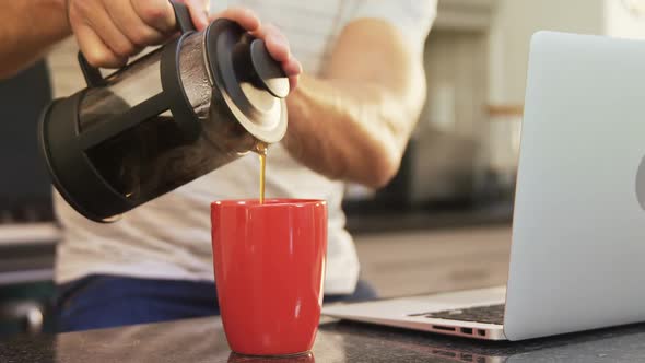 Young man pouring hot black coffee in mug