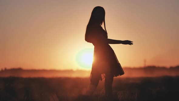 A Silhouette of a Young Girl Dancing and Spinning on a Warm Summer Evening at Sunset