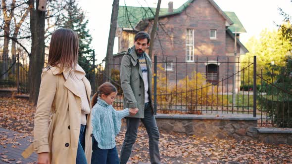 Young Parents Holding Hands of Little Daughter Talking to Her and Smiling