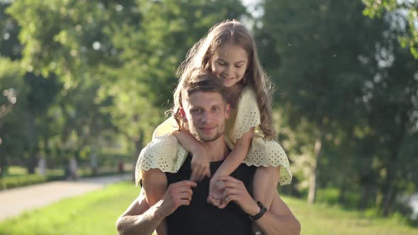 Positive Man Looking at Camera Smiling with Pretty Girl on Shoulders