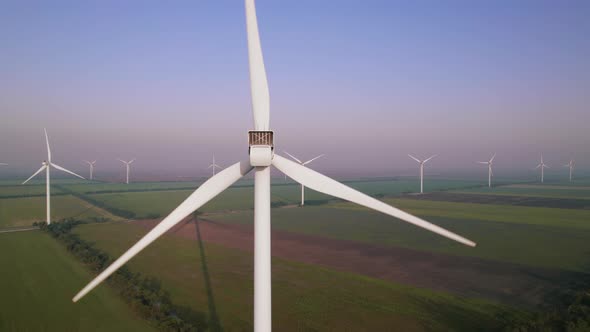 Windmills with rotating wings among green fields. Wind farm for wind energy.