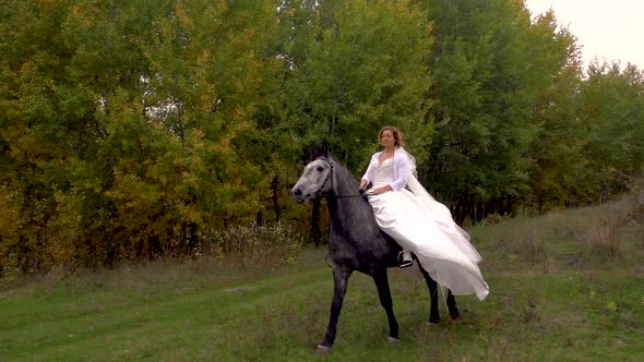 Gorgeous Fiancee in White Dress Is Riding Horse Along Forest