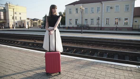 Elegant Lady Stands with Suitcase in Poses on Platform in Sunny Day