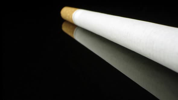 Up close view of single cigarette on black reflective surface