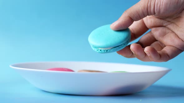 Close Up of Hand Pick Macaroon on Blue Background with Copy Space