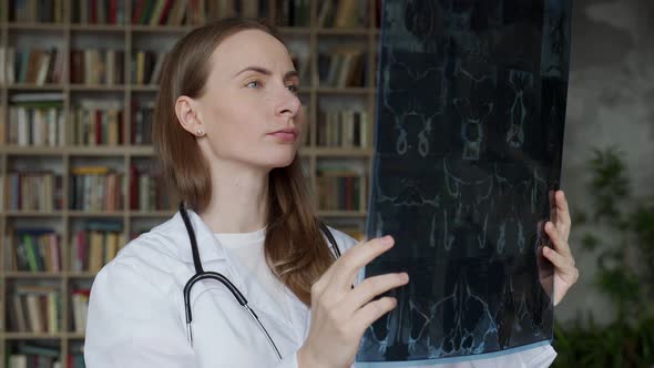 A Young Female Doctor Looks at an Xray While Sitting at a Table in the Clinic