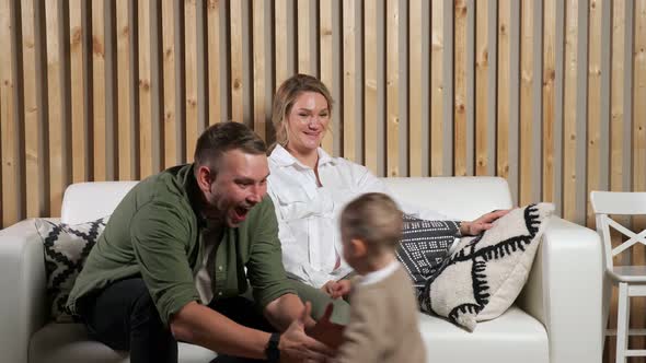Little Boy Runs to Happy Parents Sitting on White Sofa