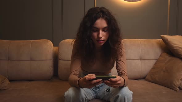 Woman Playing the Mobile Game on Phone Sitting on Couch at Home