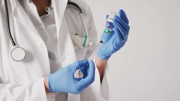 Video of biracial female doctor holding vaccine vial on white background