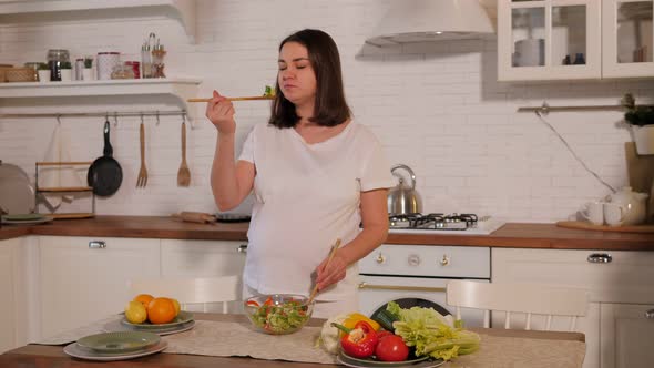 Happy Pregnant Woman Eating Fresh Vegetable Salad in the Kitchen