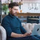 Handsome Millennial Man Working on Laptop Computer While Sitting on a Sofa in Cozy Living Room - VideoHive Item for Sale