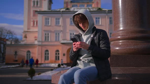 Young Man in the Hood Texting on Cell Phone Looking Around