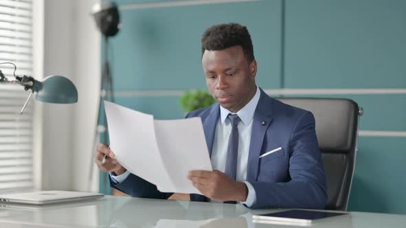 African Businessman Reading Documents While Sitting in Office