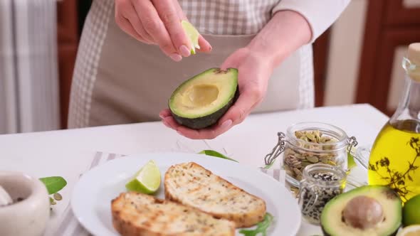 Woman Squeezing Fresh Lime Juice on Halved Avocado Fruit