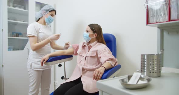 Medical Nurse in Safety Gloves and Protective Mask Is Making a Vaccine Injection To a Female Patient