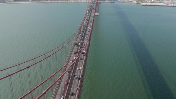 Aerial Tilt Reveal of Busy Car Traffic on Multi Lane Road Crossing Red Ponte 25 De Abril Bridge
