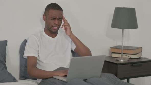 African Man with Laptop Having Headache in Bed