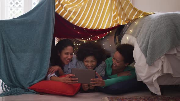 Mixed race lesbian couple and daughter using tablet lying in bedroom camp