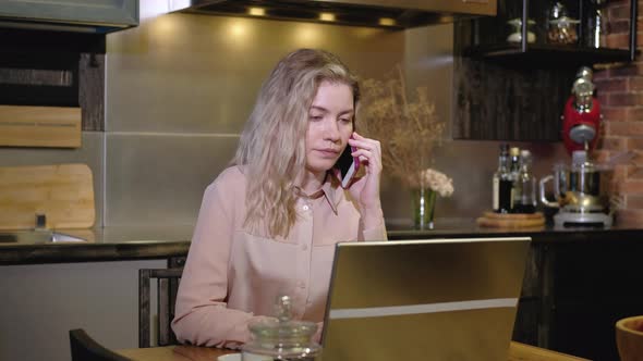 Girl in  kitchen on the phone is discussing an order with a client on a laptop