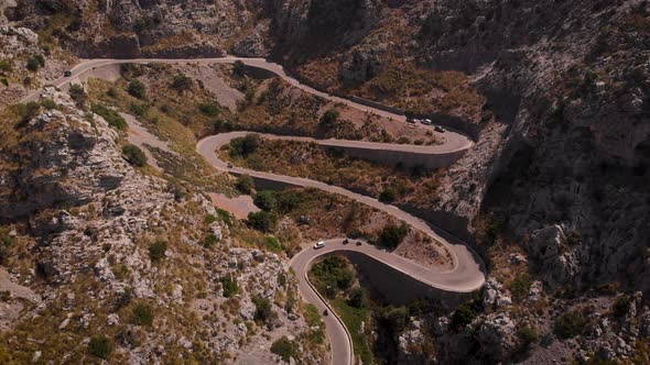 AERIAL: Cars and motorbikes on curvy serpentine road in the mountains