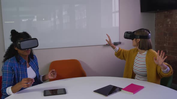 Diverse female business colleagues sitting at table using vr headsets in meeting room