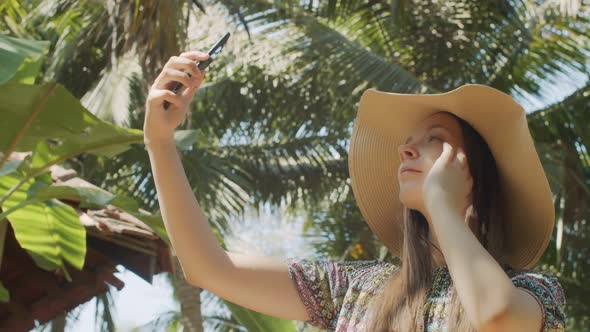 Cheerful Lady Making Selfie Photo on Mobile Phone Over Green Palm Tree Background