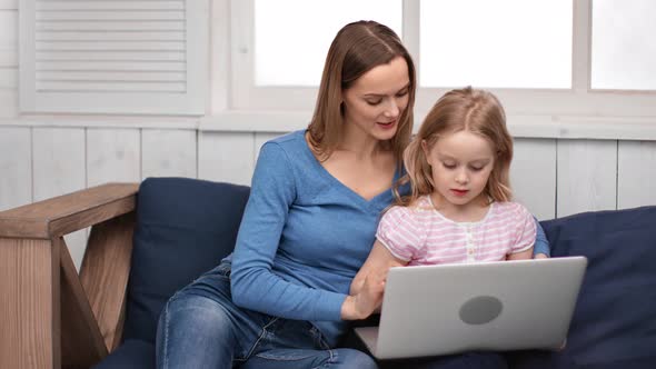 Cheerful Young Woman and Cute Little Girl Use Laptop Together