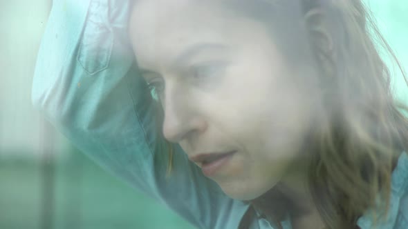 Woman leaning forehead against window, looking out in thought