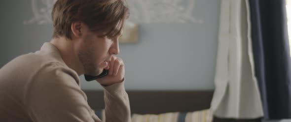 A man talking to someone on the phone while working with a laptop from home.