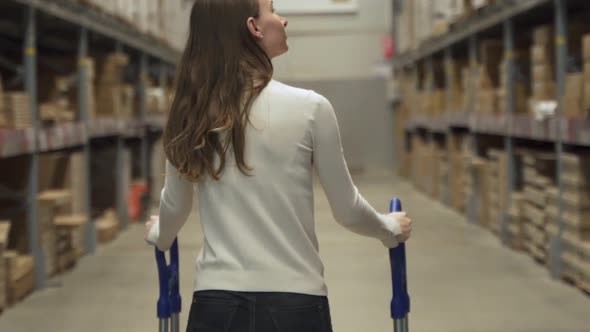 Woman Pushing a Trolley is Looking for Some Items in Warehouse