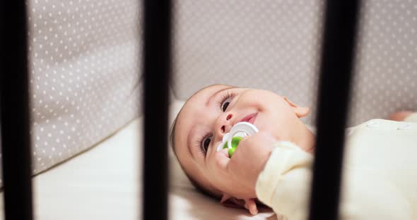 Newborn Cheerful Littlebaby is Chewing and Playing in His Crib with Nipple