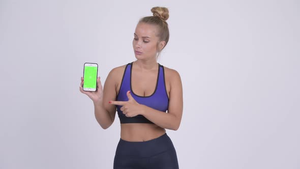 Happy Young Blonde Woman Showing Phone and Giving Thumbs Up