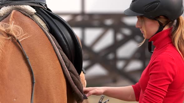 Beautiful Girl Preparing Saddle for Riding Horse