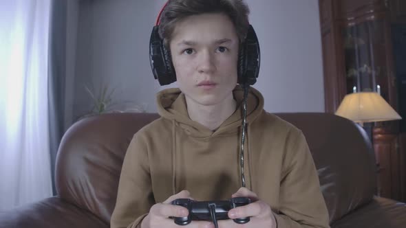 Young Brunette Boy on Headphones and Hoodie Playing Video Game. Close-up Portrait of Caucasian