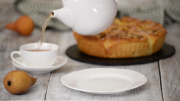 Unrecognizable Person Pouring Fresh Hot Tea Into Cup on Table and Put Bun on White Plate.