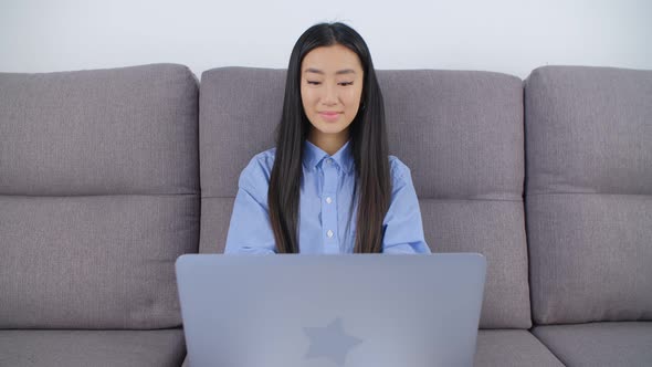 Asian girl studying online. Young woman working on computer on couch during lockdown