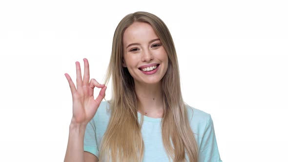 Portrait of Caucasian Blonde Woman 20s in Casual Clothing Smiling and Showing Ok Symbol with Fingers